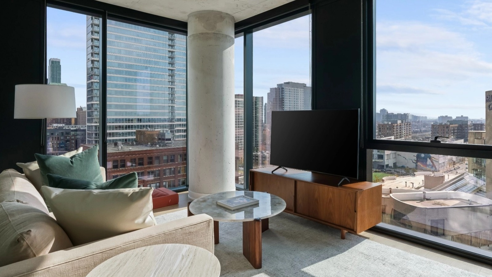 A comfortable living room with a plush sofa, stylish decor, and expansive floor-to-ceiling windows offering stunning city views at The Reed in Chicago