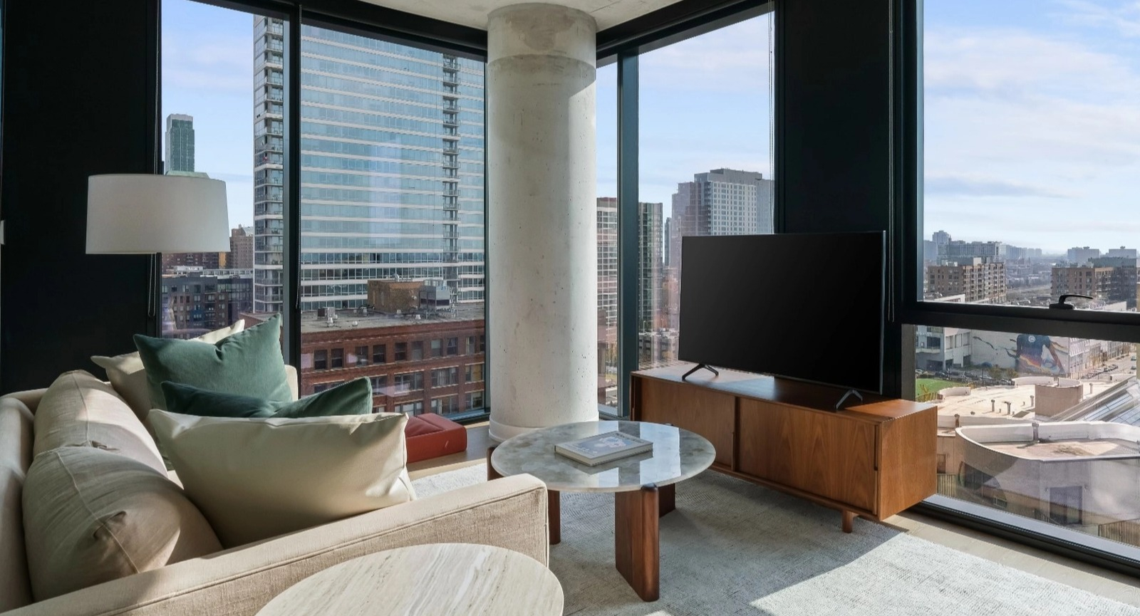 A comfortable living room with a plush sofa, stylish decor, and expansive floor-to-ceiling windows offering stunning city views at The Reed in Chicago