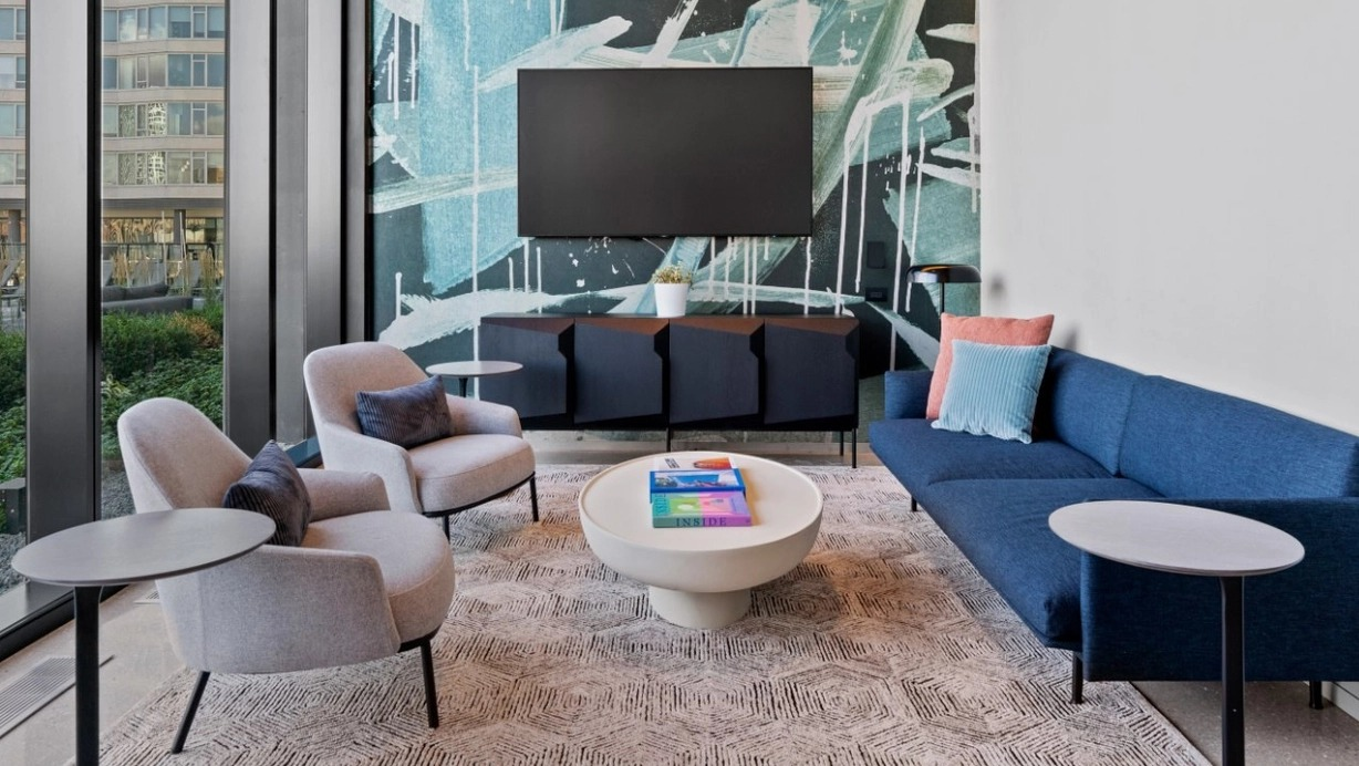 A modern resident lounge with a comfortable blue sofa, abstract wall art, and large windows providing natural light at The Reed in Chicago