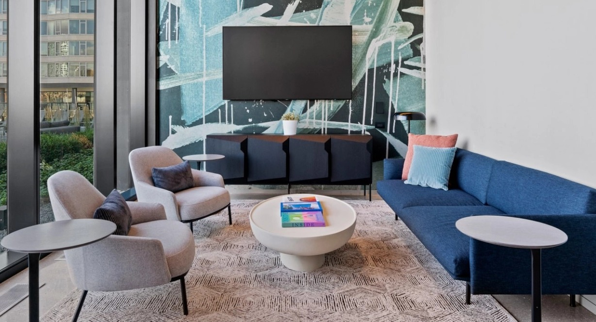 A modern resident lounge with a comfortable blue sofa, abstract wall art, and large windows providing natural light at The Reed in Chicago