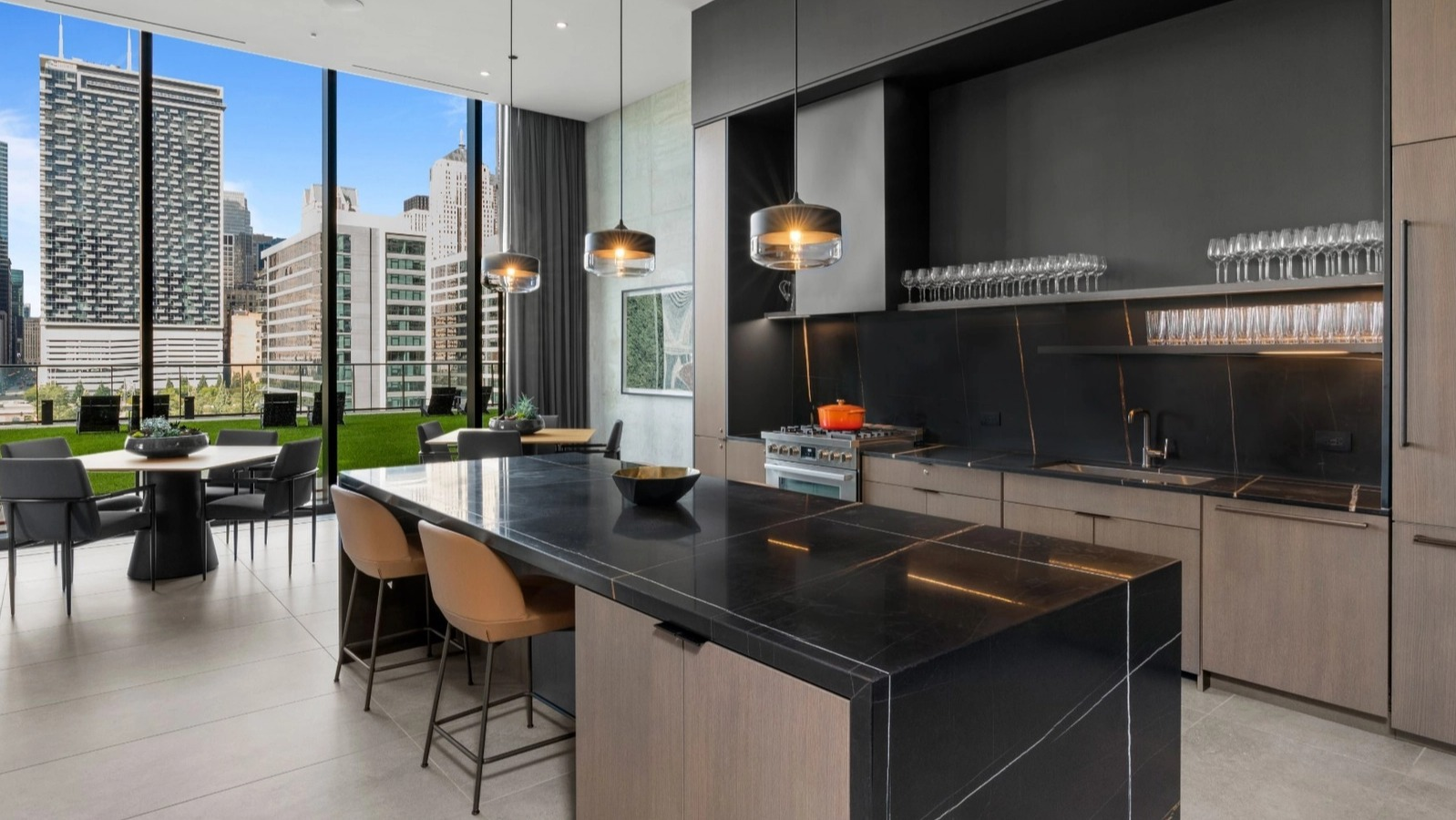 A luxurious modern kitchen with dark cabinetry, a large island, and a dining area, all with expansive city views from floor-to-ceiling windows at The Reed in Chicago