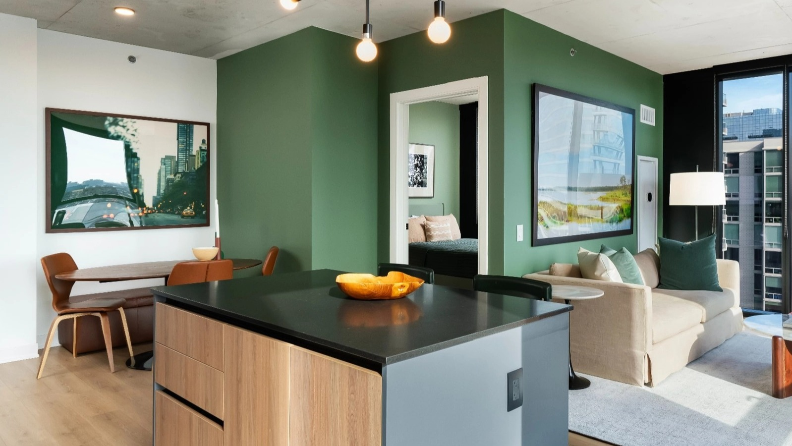 A spacious open-concept apartment featuring a modern kitchen island, dining area, and living room with a striking green accent wall at The Reed in Chicago