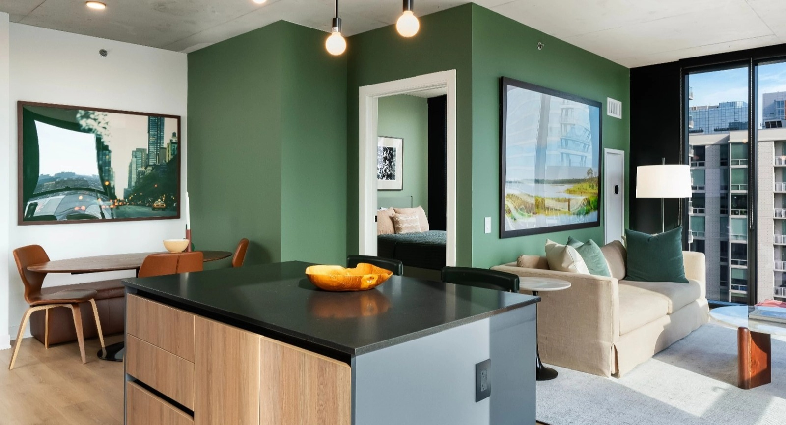A spacious open-concept apartment featuring a modern kitchen island, dining area, and living room with a striking green accent wall at The Reed in Chicago