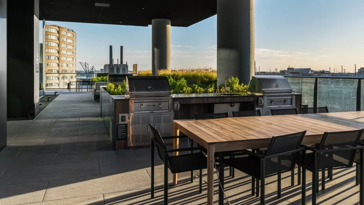 A modern outdoor patio with multiple grilling stations, large dining tables, and lush greenery, perfect for entertaining at The Reed in Chicago