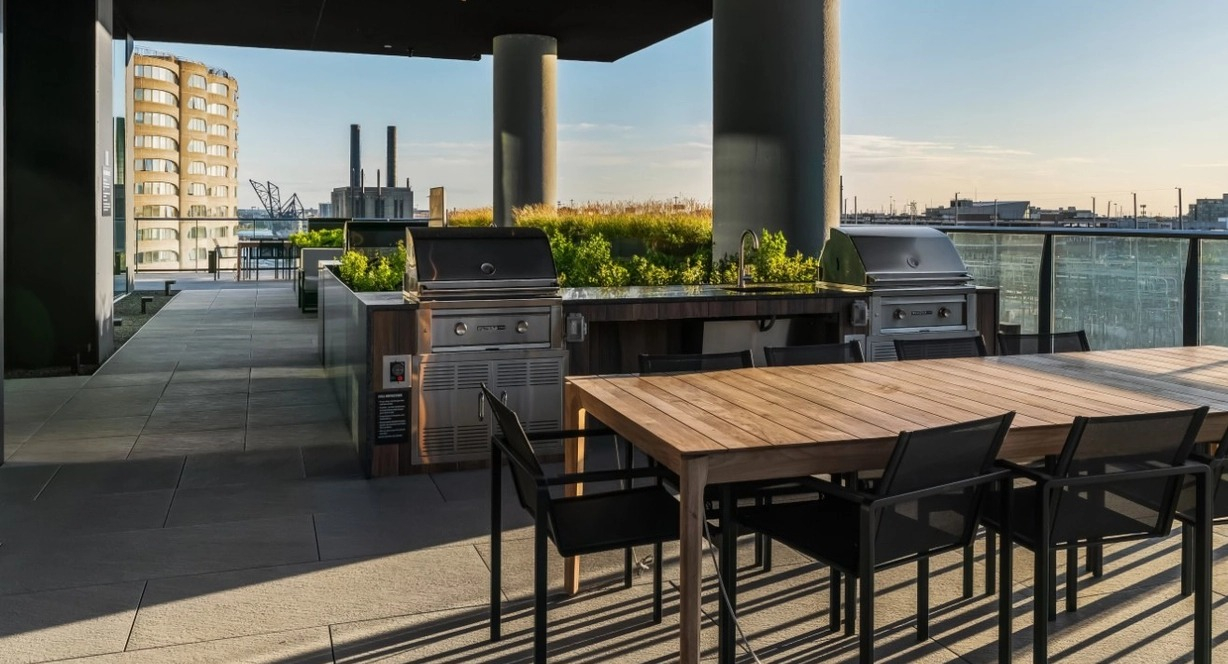 A modern outdoor patio with multiple grilling stations, large dining tables, and lush greenery, perfect for entertaining at The Reed in Chicago