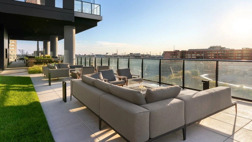A luxurious outdoor lounge area with comfortable sectional sofas and glass railings, offering stunning cityscape views at The Reed in Chicago