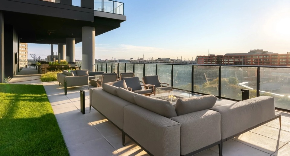A luxurious outdoor lounge area with comfortable sectional sofas and glass railings, offering stunning cityscape views at The Reed in Chicago
