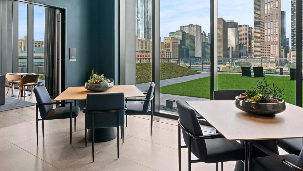A chic resident lounge with dining tables and comfortable seating, offering spectacular views of the Chicago skyline at The Reed in Chicago