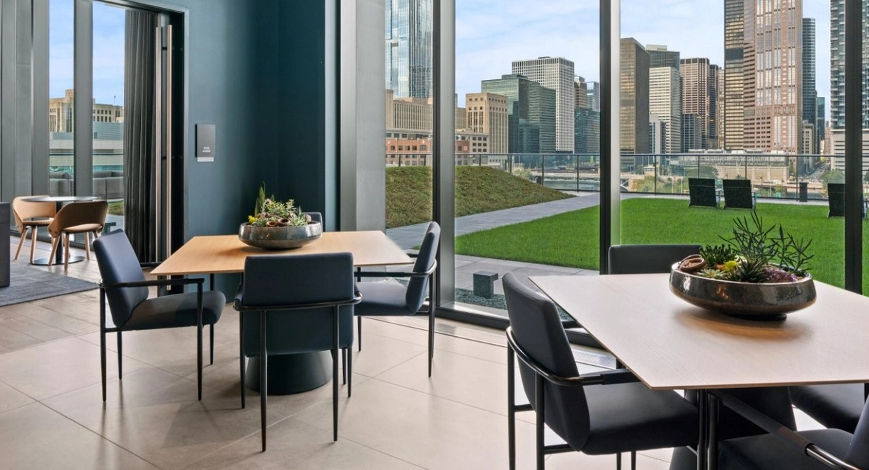 A chic resident lounge with dining tables and comfortable seating, offering spectacular views of the Chicago skyline at The Reed in Chicago
