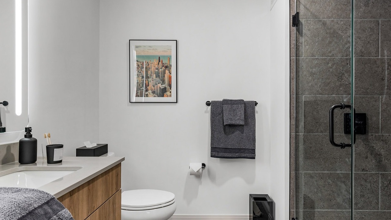 Contemporary bathroom with a modern vanity, illuminated mirror, toilet, and a spacious walk-in shower at The Saint Grand in Chicago