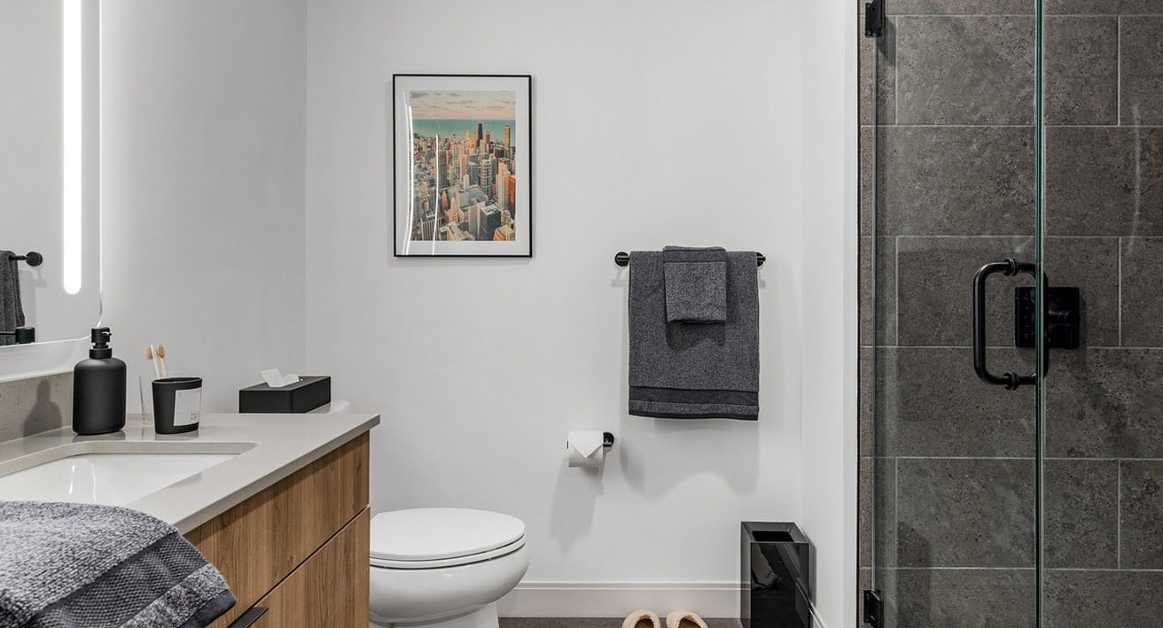 Contemporary bathroom with a modern vanity, illuminated mirror, toilet, and a spacious walk-in shower at The Saint Grand in Chicago