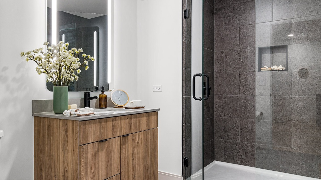 Modern bathroom at The Saint Grand in Chicago, featuring a sleek wooden vanity, illuminated mirror, and a spacious walk-in shower