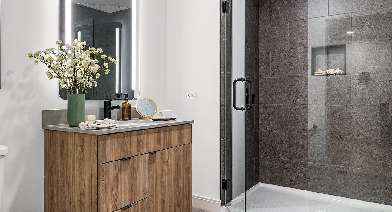 Modern bathroom at The Saint Grand in Chicago, featuring a sleek wooden vanity, illuminated mirror, and a spacious walk-in shower