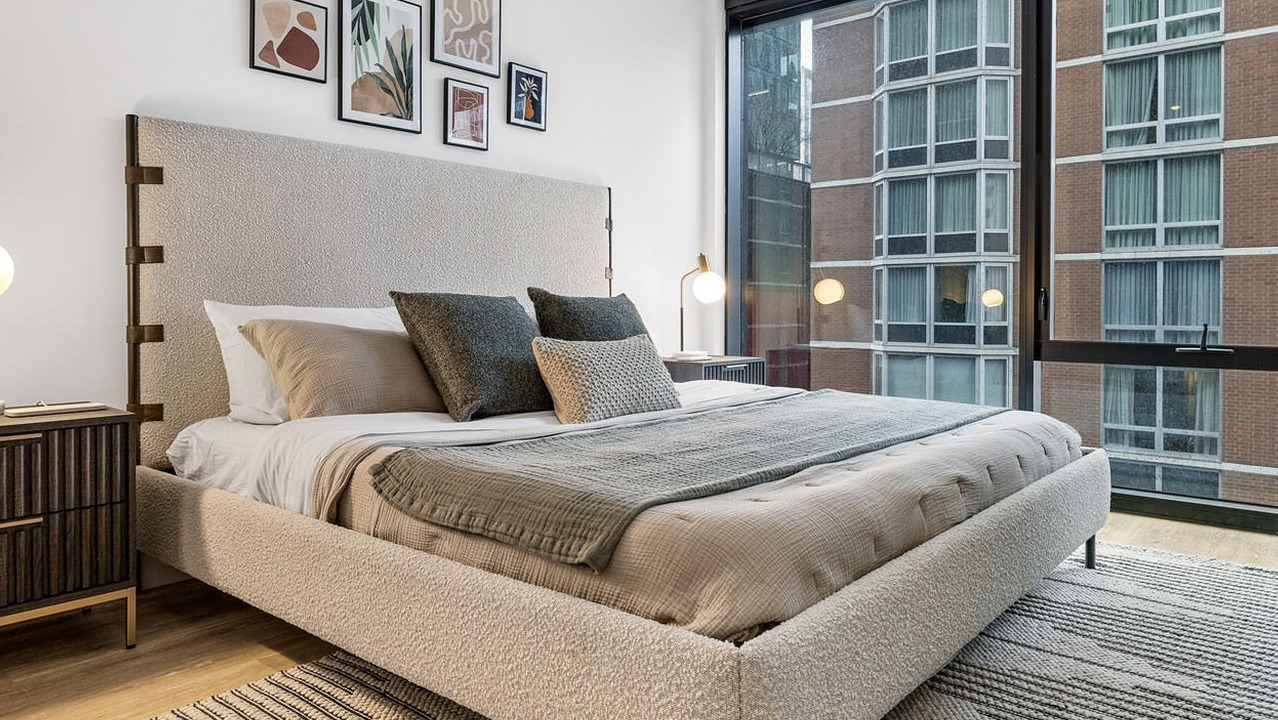 Cozy bedroom at The Saint Grand in Chicago, featuring a comfortable bed, warm lighting, and large windows with urban views