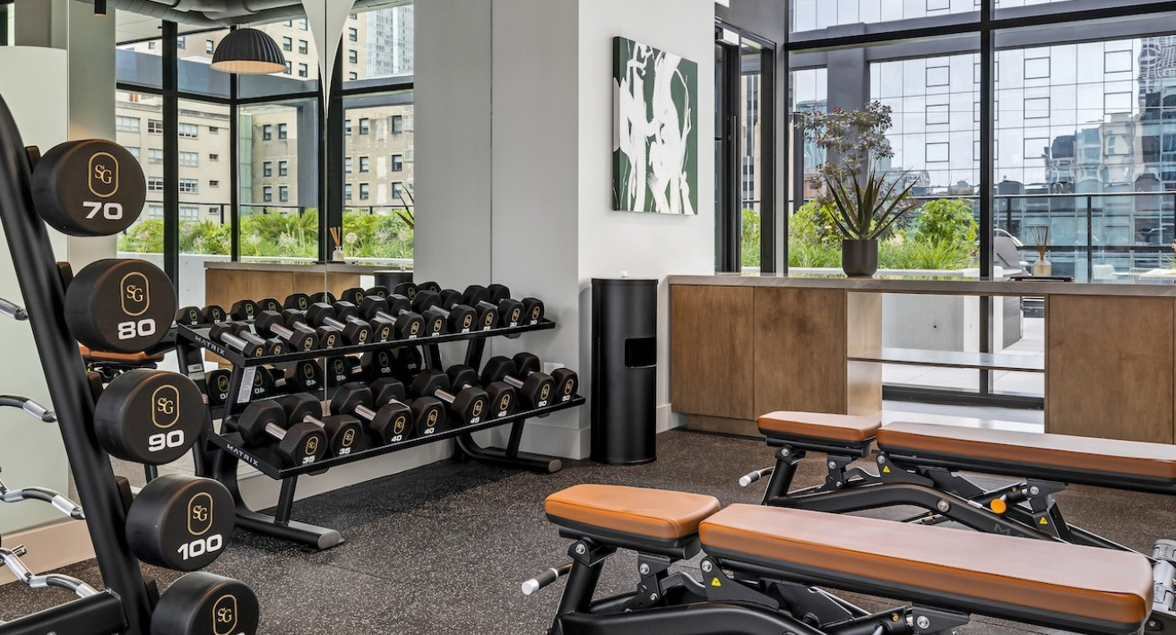 Modern fitness center at The Saint Grand in Chicago, featuring a wide selection of free weights, benches, and ample workout space