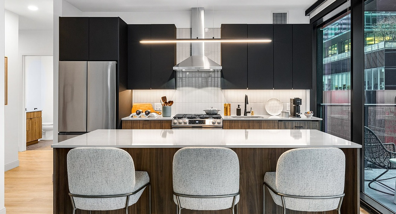 Modern kitchen at The Saint Grand in Chicago, featuring an island, sleek black cabinetry, stainless steel appliances, and a balcony