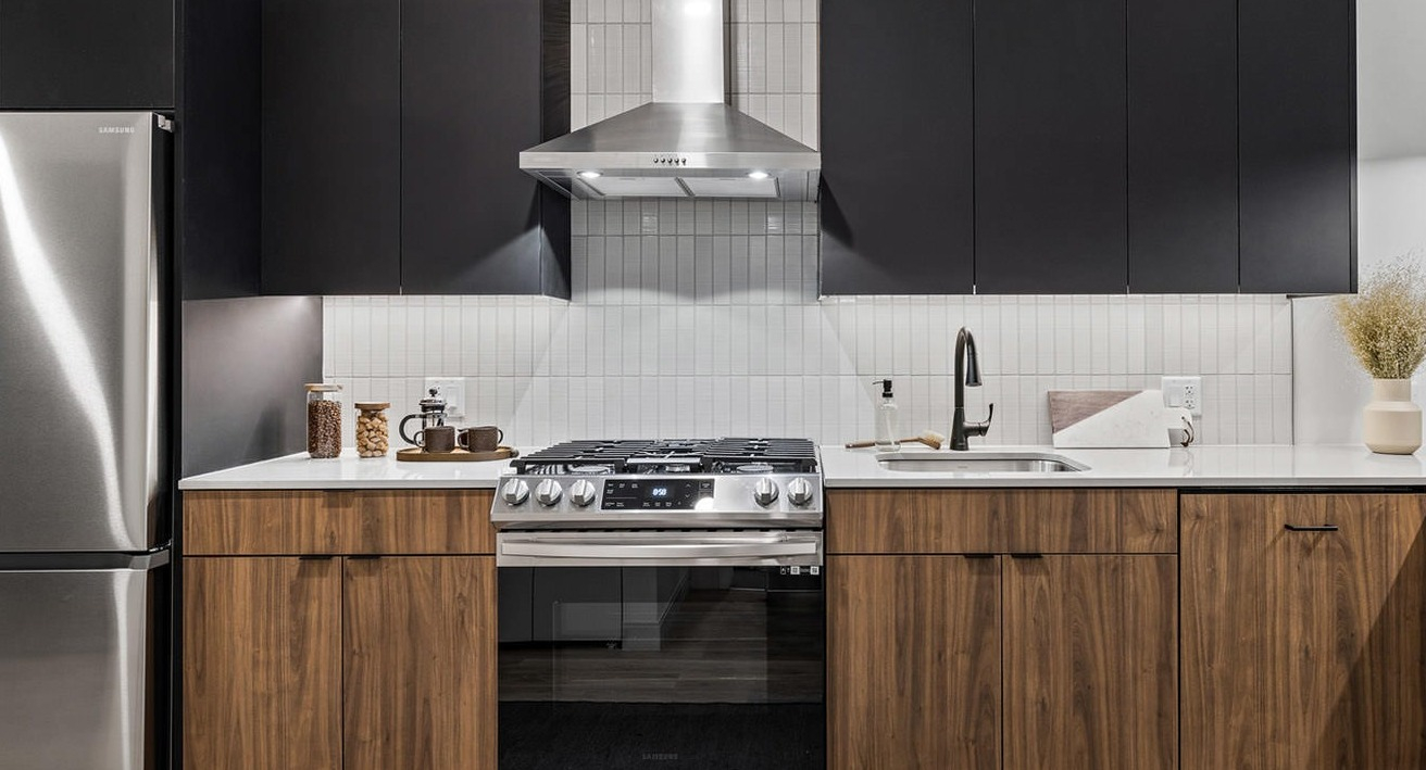 Modern kitchen featuring two-tone cabinetry (dark and wood), stainless steel appliances, and sleek design at The Saint Grand in Chicago