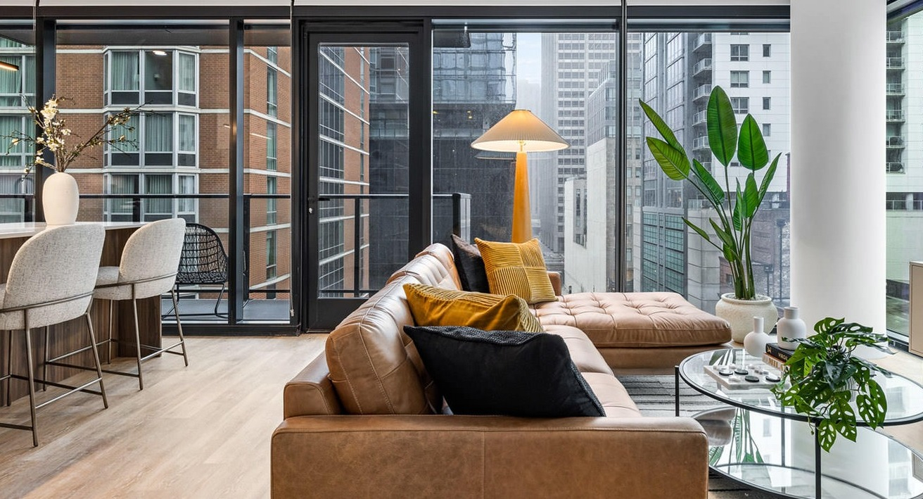 Bright living room at The Saint Grand in Chicago, featuring a comfortable leather sofa, modern decor, and a balcony with city views