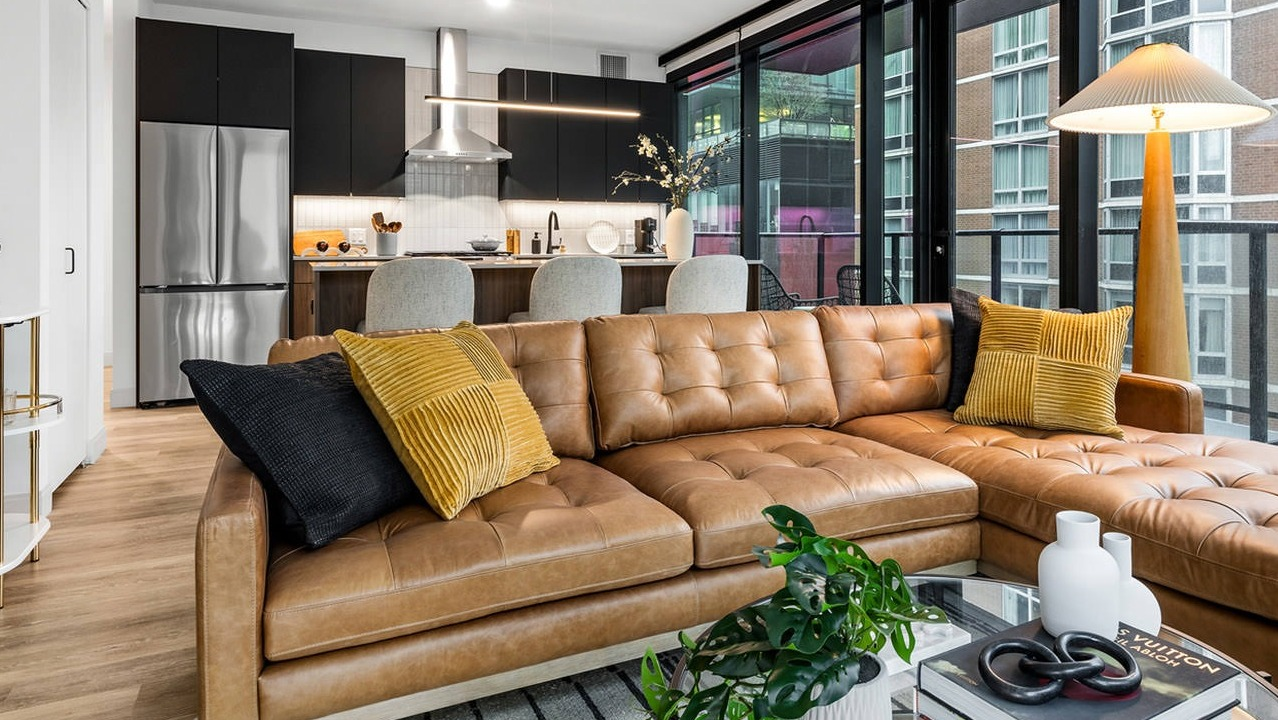 Open-concept living room and kitchen at The Saint Grand in Chicago, featuring a stylish leather sofa, modern kitchen, and balcony access