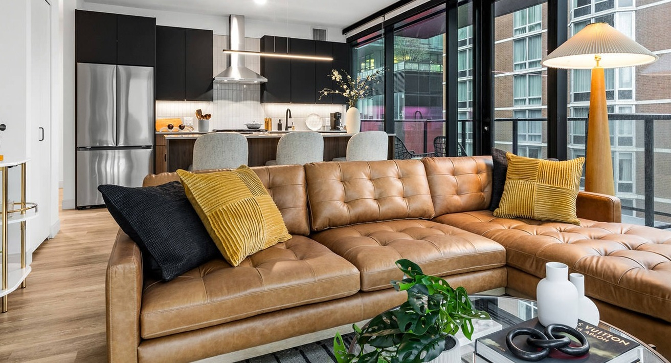 Open-concept living room and kitchen at The Saint Grand in Chicago, featuring a stylish leather sofa, modern kitchen, and balcony access