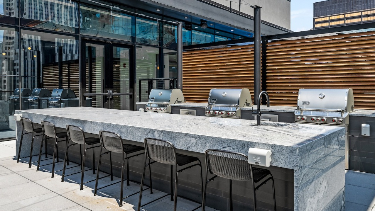 Expansive rooftop grilling station with multiple grills, a large island for dining, and cityscape views at The Saint Grand in Chicago