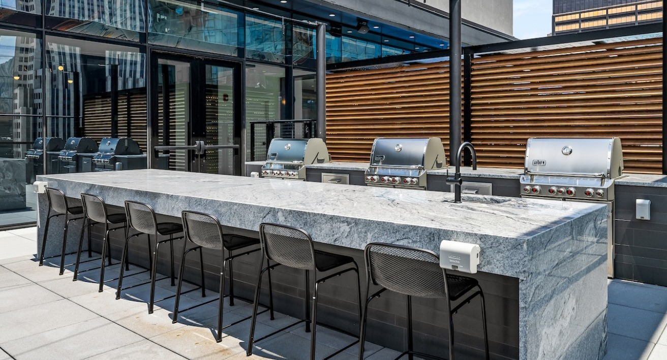 Expansive rooftop grilling station with multiple grills, a large island for dining, and cityscape views at The Saint Grand in Chicago