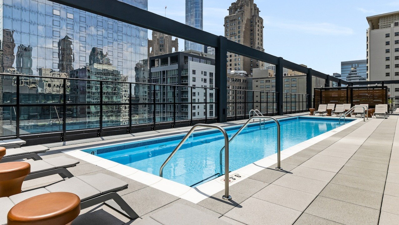 Luxurious rooftop pool deck at The Saint Grand in Chicago, featuring a sparkling pool, lounge chairs, and a stunning cityscape