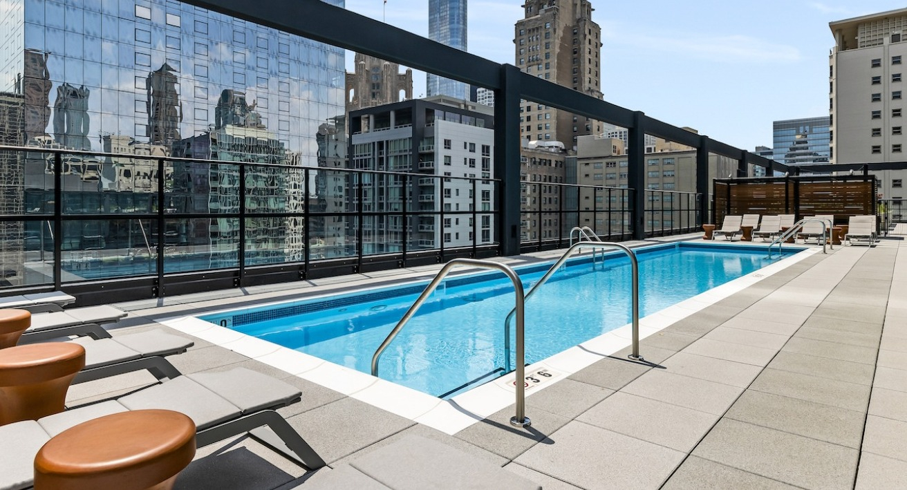 Luxurious rooftop pool deck at The Saint Grand in Chicago, featuring a sparkling pool, lounge chairs, and a stunning cityscape