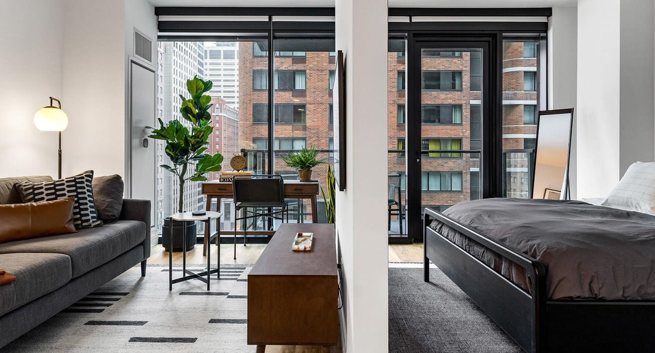 Thoughtfully designed studio apartment with distinct living and sleeping areas, modern furniture, and large windows at The Saint Grand in Chicago