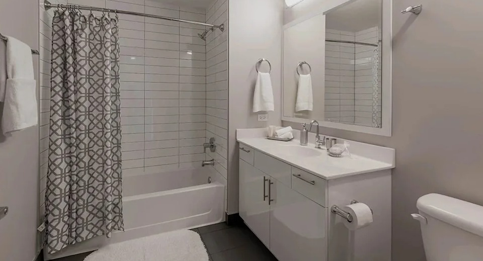 Clean and modern bathroom with a white vanity, spacious mirror, and a shower-over-tub combo at The Scott Residences in Chicago