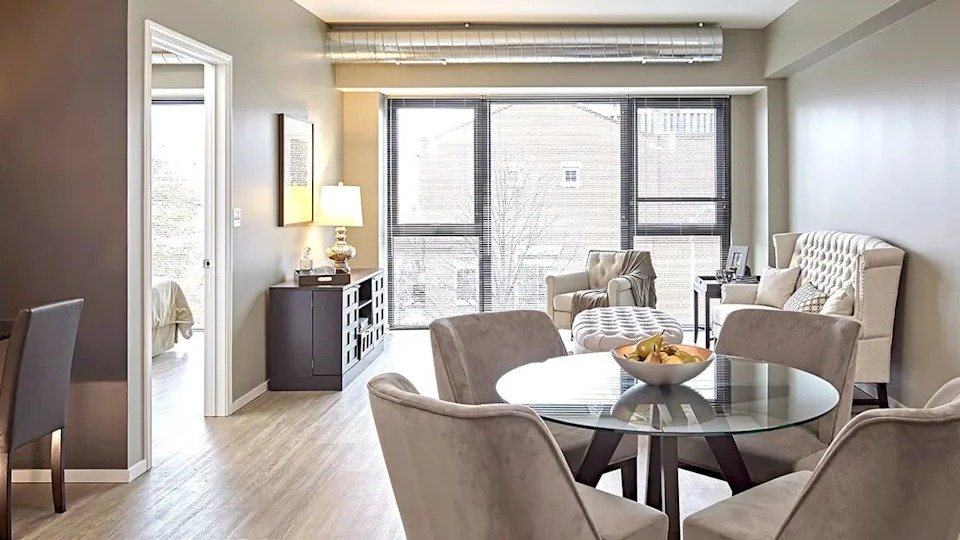Open-concept dining and living area with a round glass table, neutral decor, and large windows at The Scott Residences in Chicago