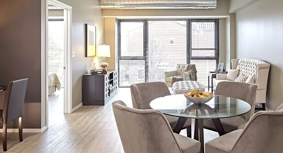 Open-concept dining and living area with a round glass table, neutral decor, and large windows at The Scott Residences in Chicago