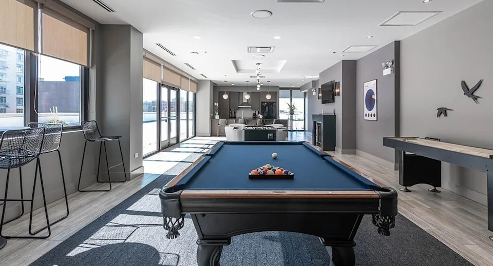 Lively game room featuring a billiards table, shuffleboard, and bar seating, offering entertainment for residents at The Scott Residences in Chicago