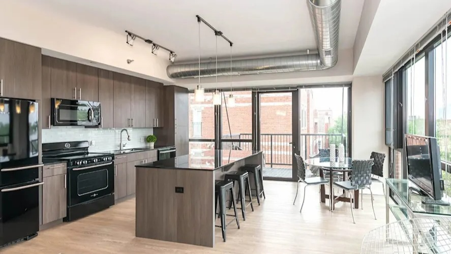 Bright open-concept kitchen and dining area with modern appliances, a large island, and industrial-chic exposed ductwork at The Scott Residences in Chicago