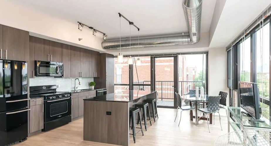 Bright open-concept kitchen and dining area with modern appliances, a large island, and industrial-chic exposed ductwork at The Scott Residences in Chicago