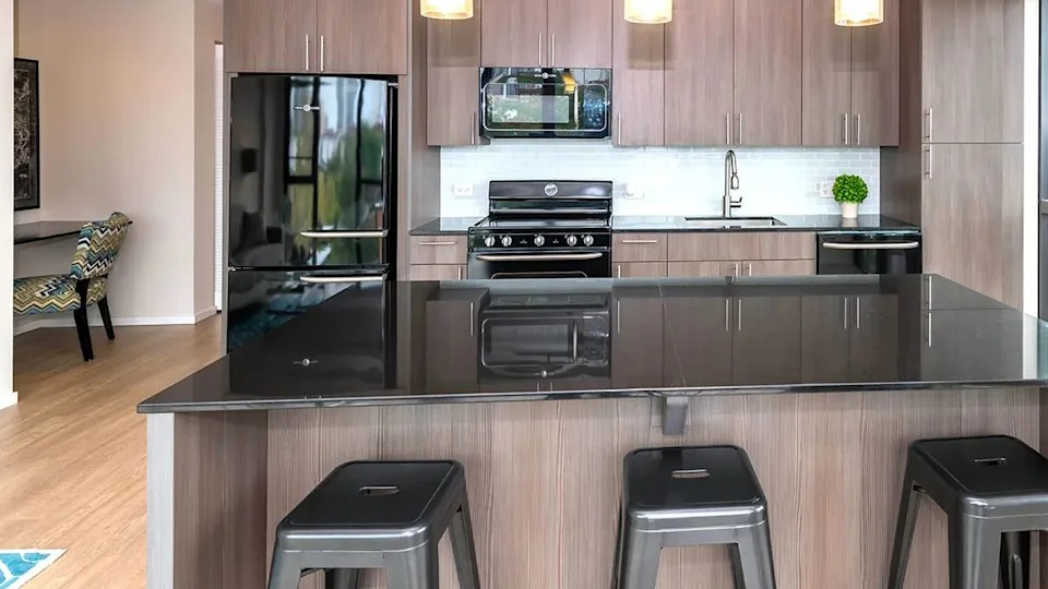 Modern kitchen with dark wood cabinets, black appliances, a large island with bar seating, and pendant lights at The Scott Residences in Chicago