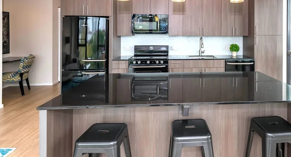 Modern kitchen with dark wood cabinets, black appliances, a large island with bar seating, and pendant lights at The Scott Residences in Chicago