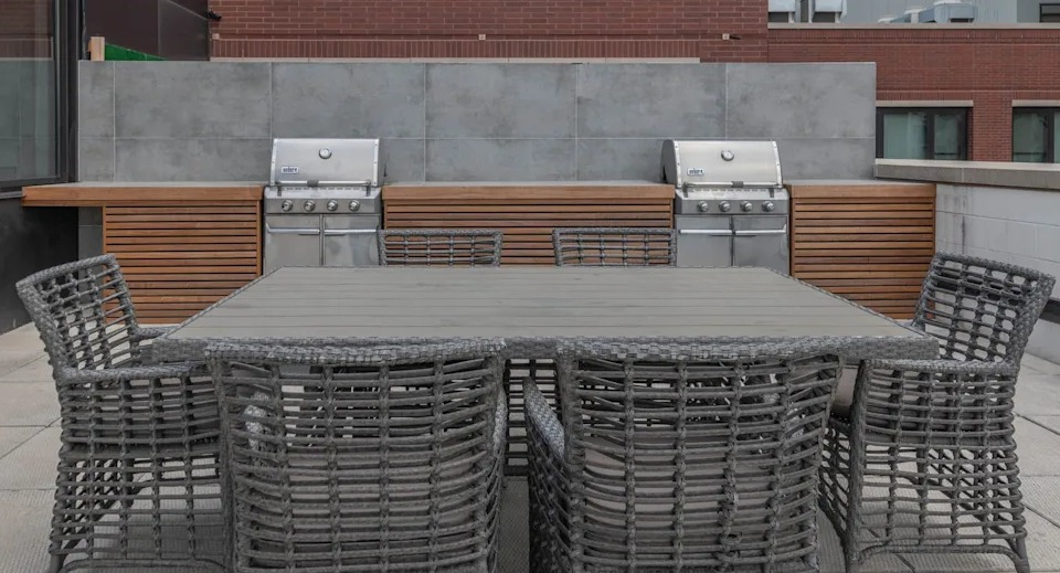 Outdoor rooftop dining area with a large table, comfortable chairs, and multiple grilling stations at The Scott Residences in Chicago