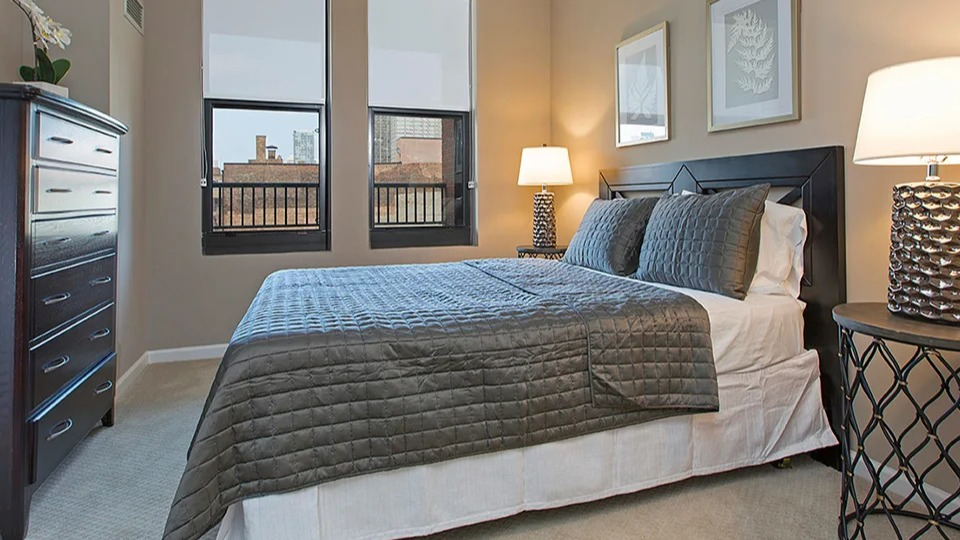 Comfortable bedroom at The Shelby in Chicago, featuring a cozy bed, dark wood furniture, and a ceiling fan for comfort