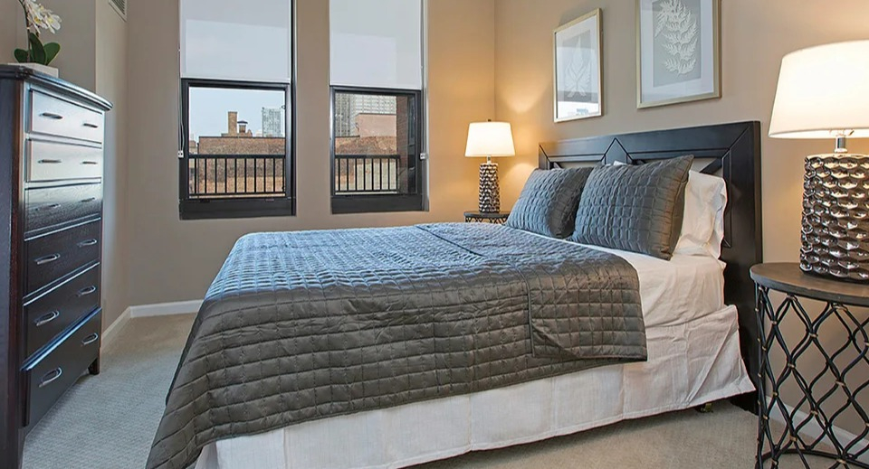 Comfortable bedroom at The Shelby in Chicago, featuring a cozy bed, dark wood furniture, and a ceiling fan for comfort