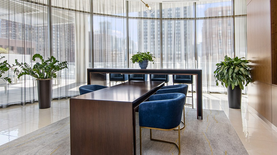 A modern resident conference room with a large table, blue velvet chairs, and vibrant artwork, ideal for meetings or study at The Sinclair in Chicago