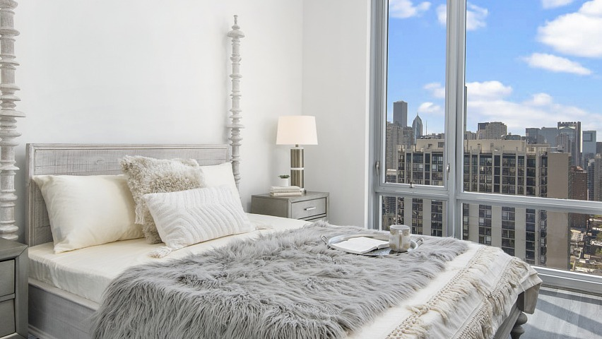 A chic and cozy bedroom with a comfortable bed, bedside tables, and a large window presenting captivating city views at The Sinclair in Chicago