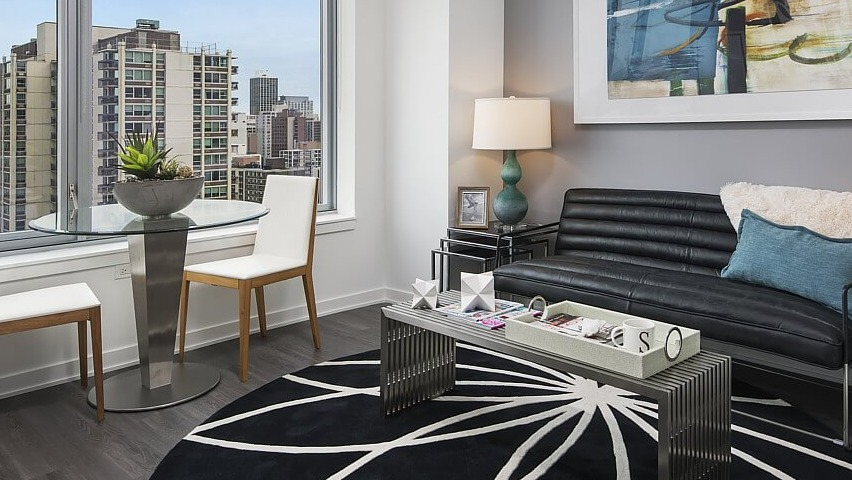 A charming apartment living area with a comfortable sofa, round dining table, and large windows offering scenic city views at The Sinclair in Chicago