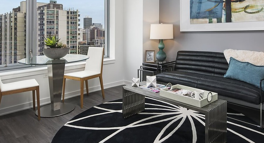 A charming apartment living area with a comfortable sofa, round dining table, and large windows offering scenic city views at The Sinclair in Chicago