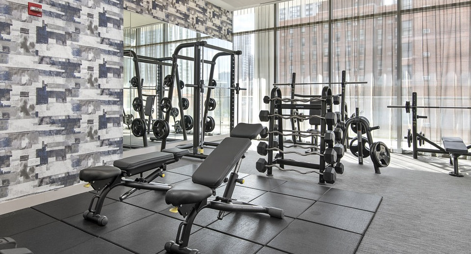 A modern fitness center with ample space for strength training, featuring free weights, benches, and power racks at The Sinclair in Chicago
