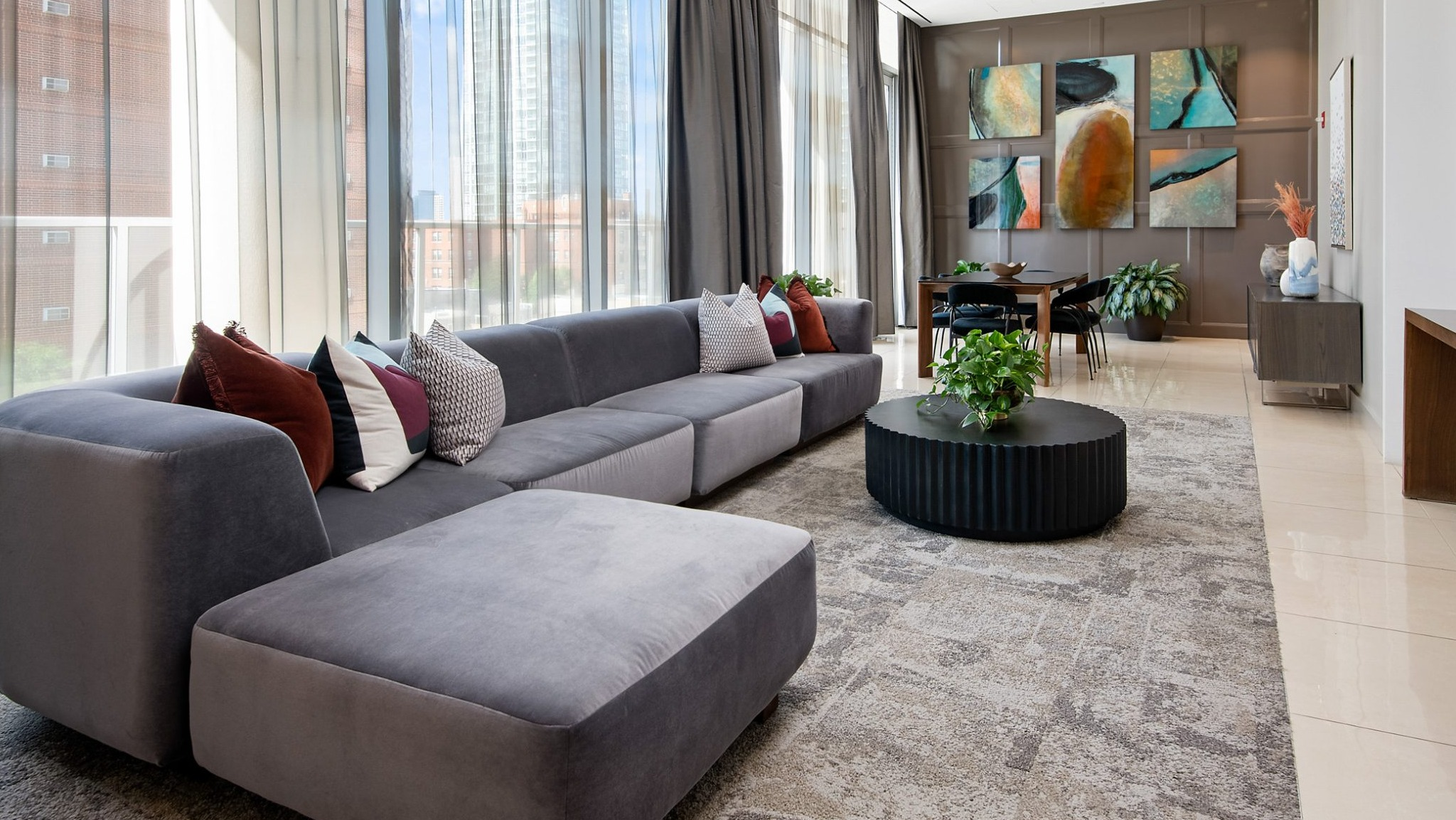 A grand resident lounge featuring an oversized sectional sofa, modern decor, a dining area, and large windows overlooking the city at The Sinclair in Chicago