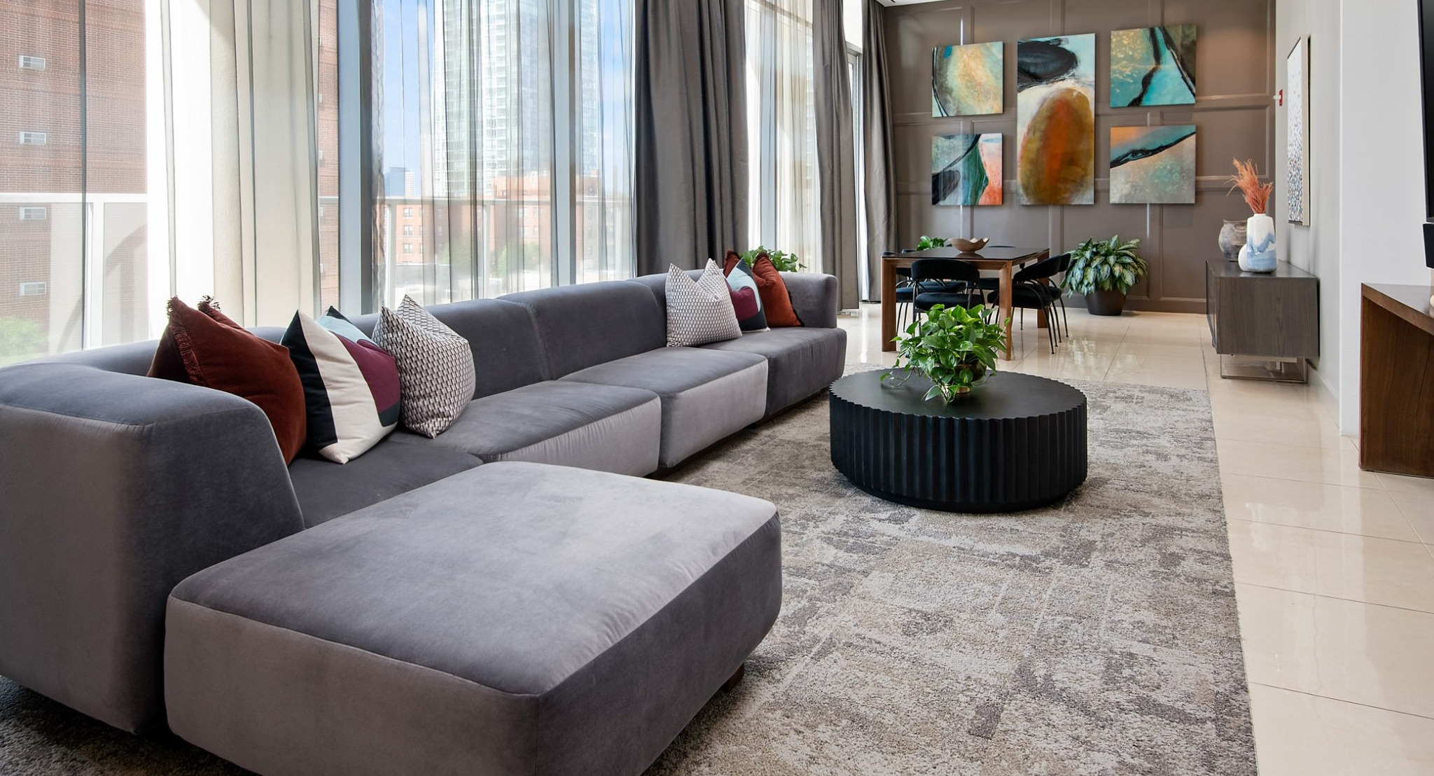 A grand resident lounge featuring an oversized sectional sofa, modern decor, a dining area, and large windows overlooking the city at The Sinclair in Chicago
