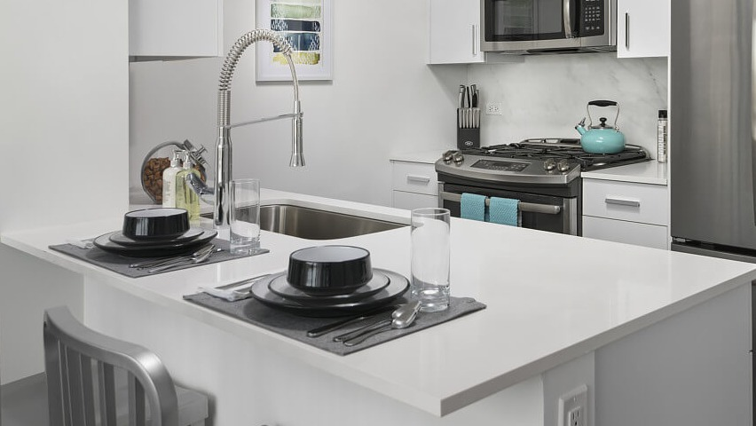 A close-up of a modern kitchen island with bar seating, white countertops, and stainless steel appliances at The Sinclair apartments in Chicago