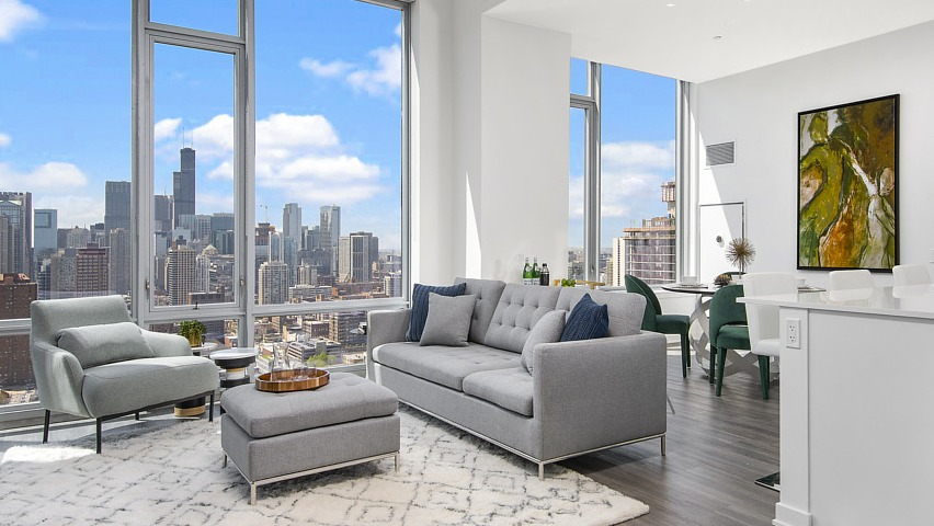 A luxurious apartment living room with a comfortable sofa, modern decor, and stunning Chicago skyline views from large windows at The Sinclair in Chicago