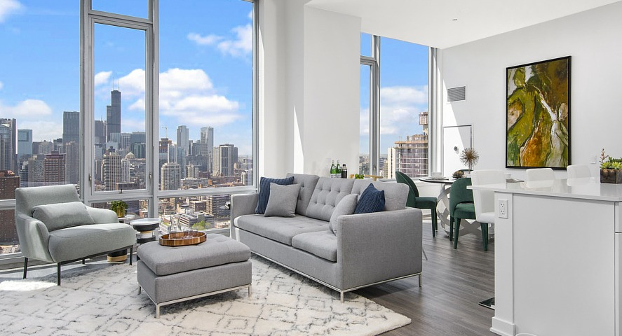 A luxurious apartment living room with a comfortable sofa, modern decor, and stunning Chicago skyline views from large windows at The Sinclair in Chicago